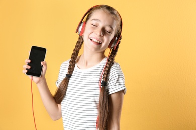 Photo of Cute little girl listening to music with headphones on color background