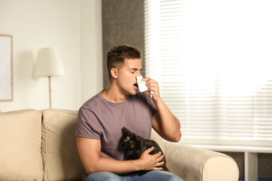 Photo of Young man with cat suffering from allergy at home