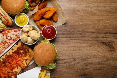 French fries, burgers and other fast food on wooden table, flat lay with space for text