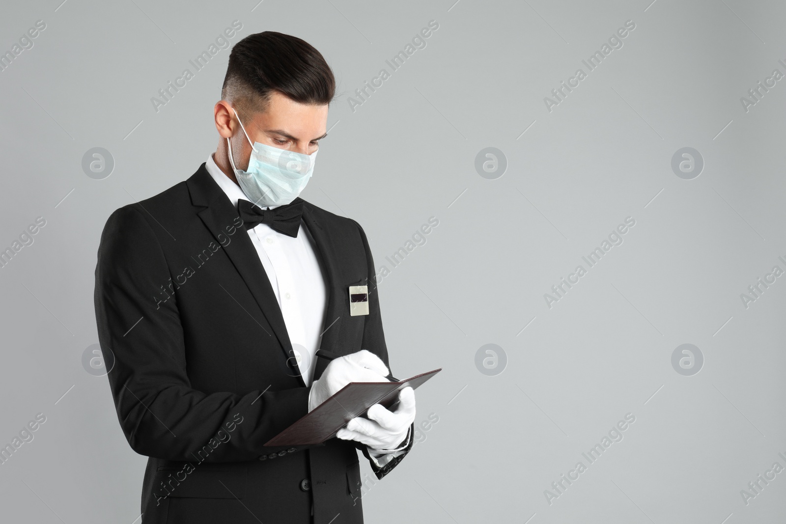 Photo of Waiter in medical face mask taking order on light grey background. Space for text