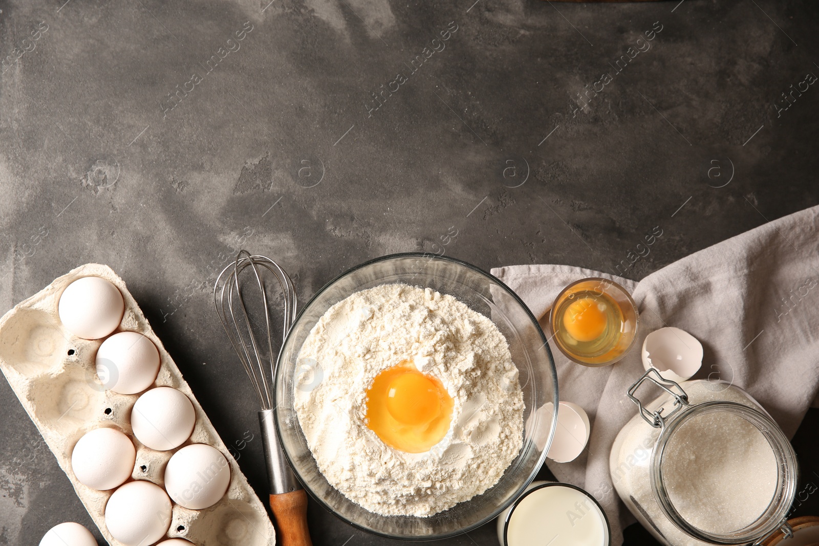 Photo of Making dough. Flour with egg yolk in bowl and other products on grey textured table, flat lay. Space for text