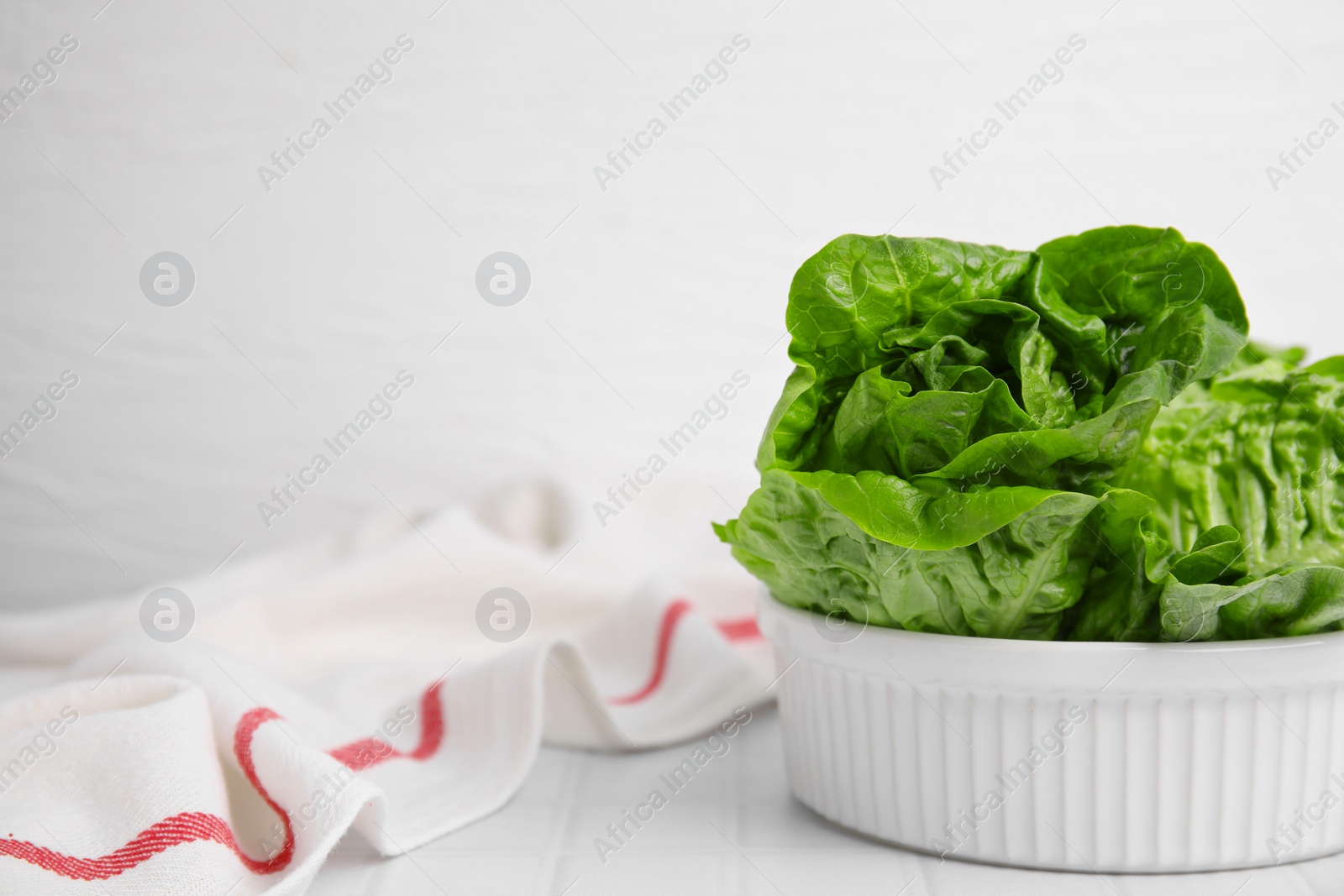 Photo of Bowl with fresh green romaine lettuces on white tiled table, space for text