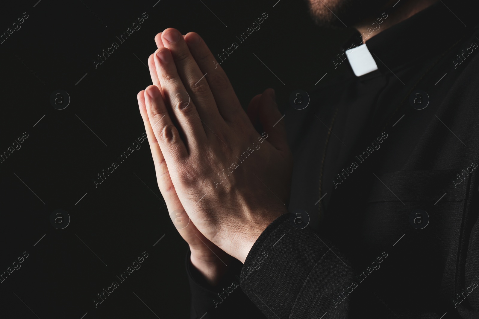 Photo of Priest in cassock praying on dark background, closeup