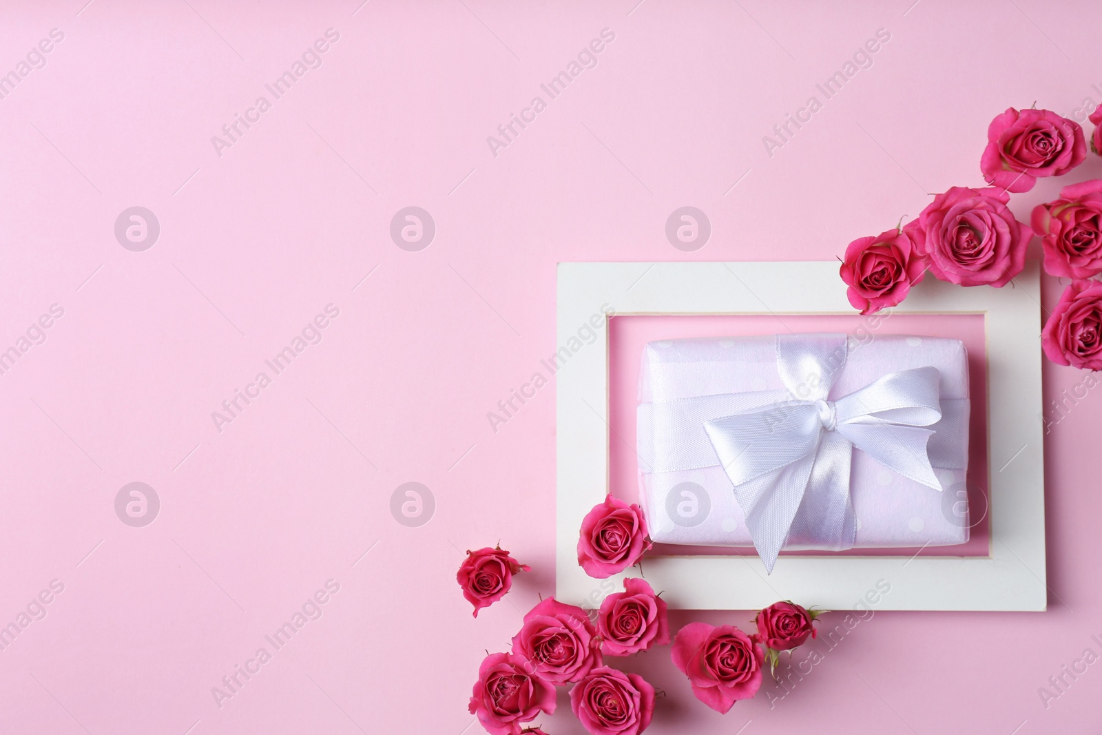 Photo of Frame with roses and gift box on color background, top view. Space for text