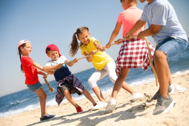 Photo of Cute children pulling rope during tug of war game on beach. Summer camp