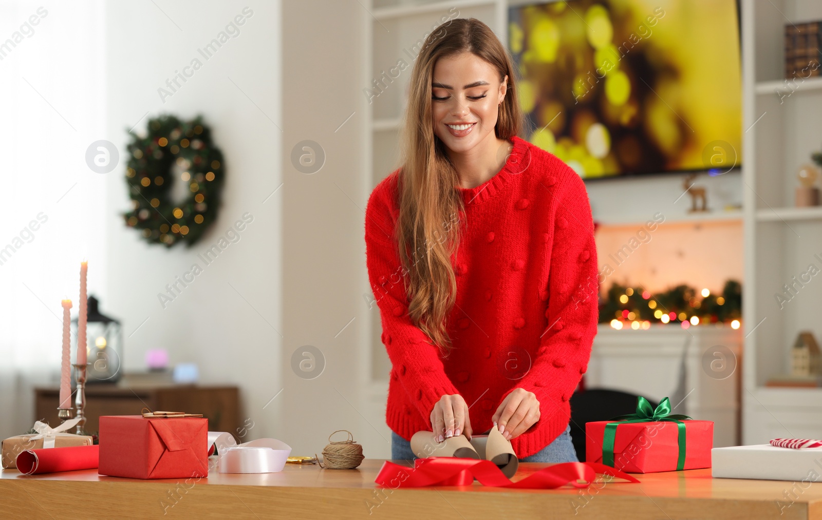 Photo of Beautiful young woman decorating Christmas gift at table in room