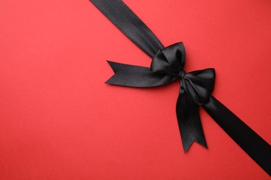 Photo of Black satin ribbon with bow on red background, top view. Space for text