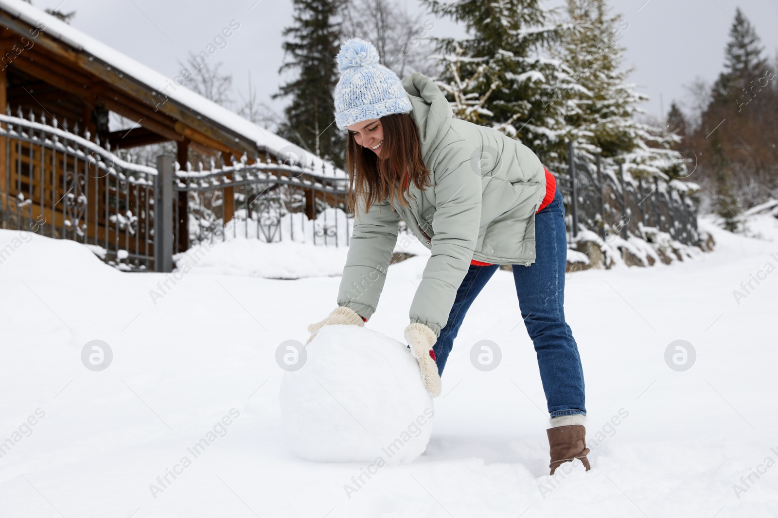 Photo of Happy woman making ball for snowman outdoors. Winter vacation