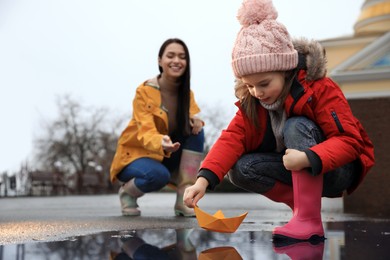 Photo of Little girl and her mother playing with paper boat near puddle outdoors