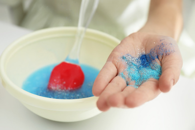 Little girl adding colored sparkles to homemade slime toy at table, closeup