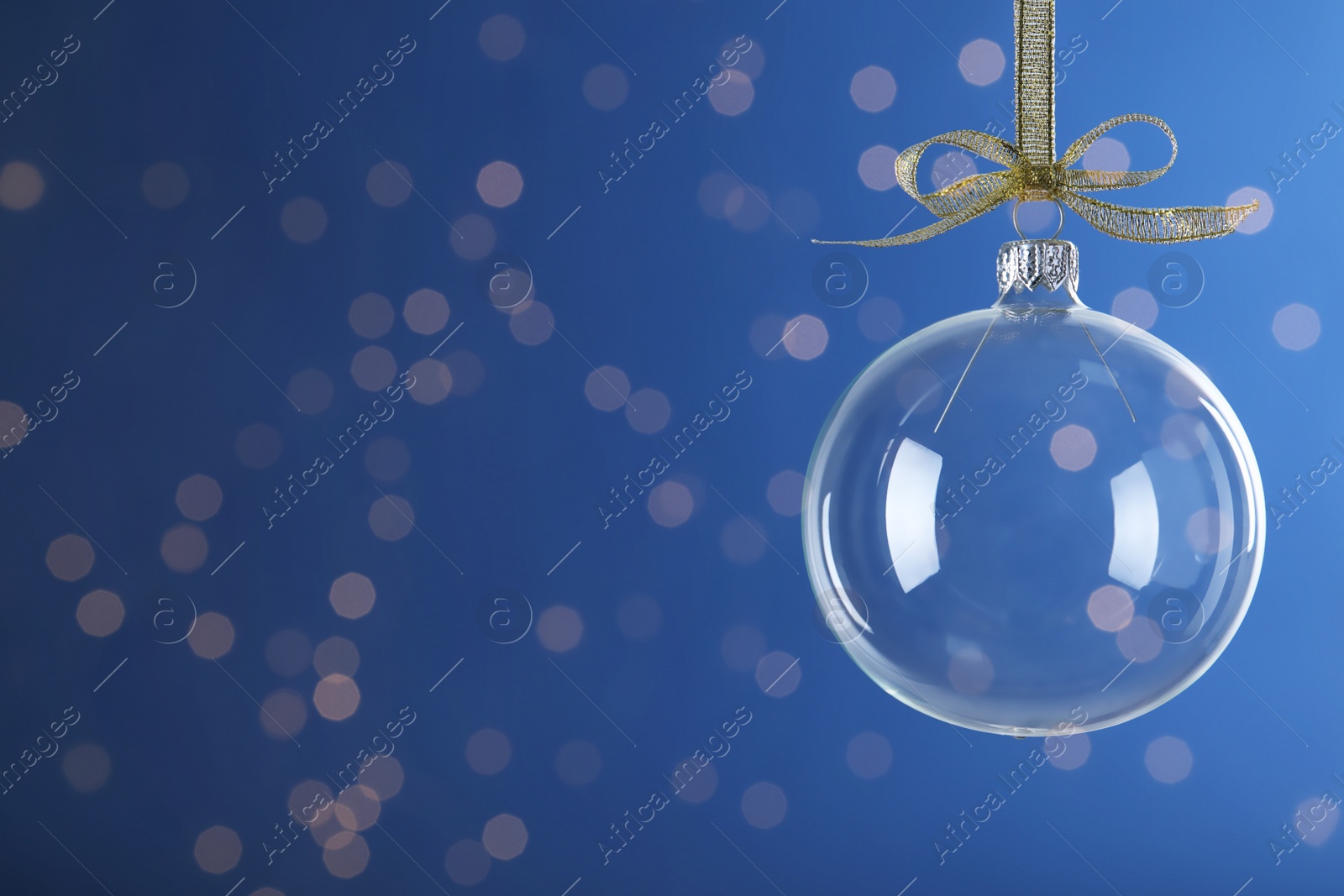 Photo of Transparent glass Christmas ball with golden ribbon and bow against blue background. Space for text