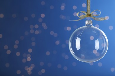 Photo of Transparent glass Christmas ball with golden ribbon and bow against blue background. Space for text