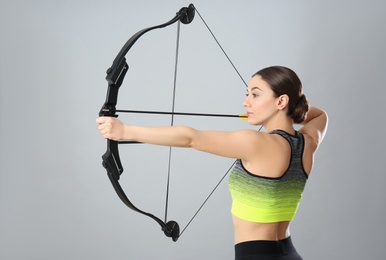 Photo of Sporty young woman practicing archery on light grey background