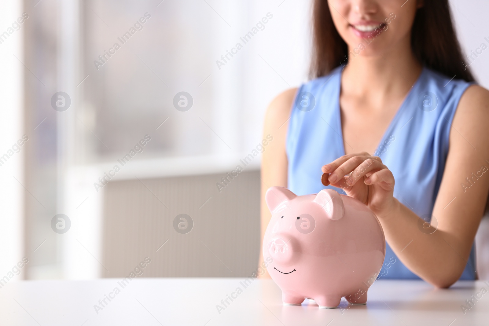 Photo of Woman putting coin into piggy bank at table indoors, closeup. Space for text