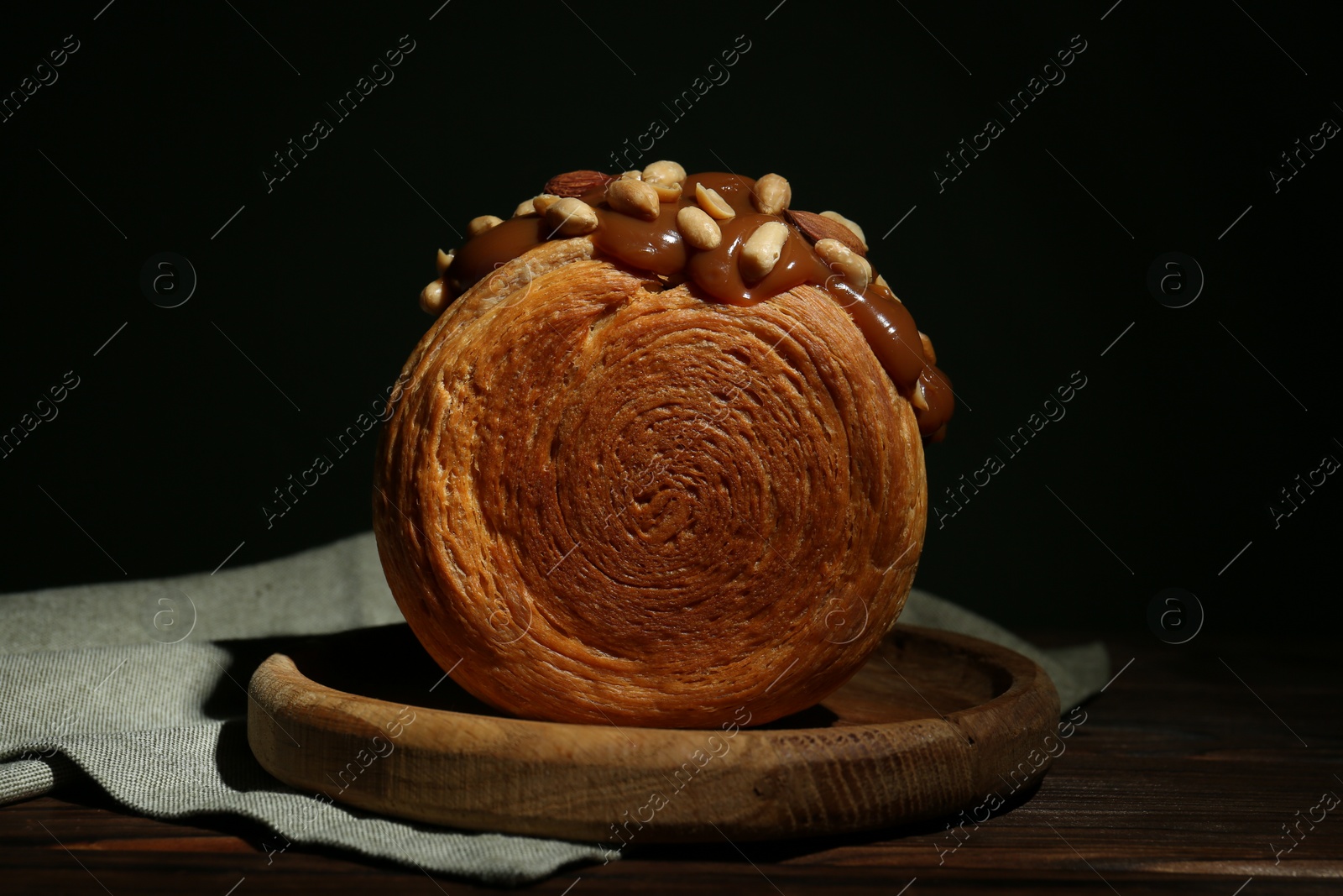 Photo of Round croissant with chocolate paste and nuts on wooden table. Tasty puff pastry