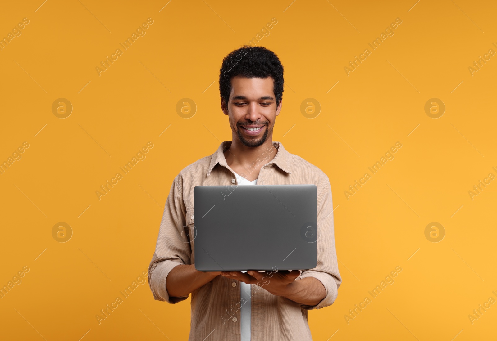 Photo of Happy man using laptop on orange background