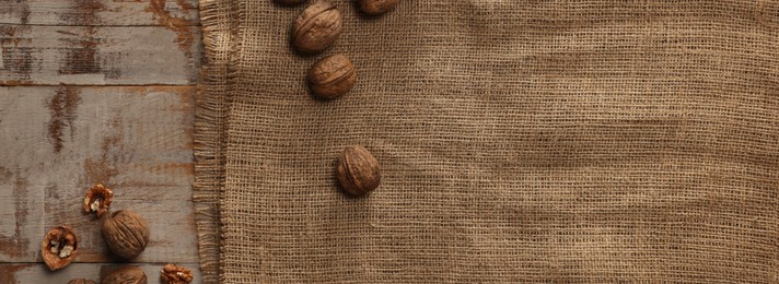 Photo of Burlap fabric and walnuts on wooden table, top view. Space for text