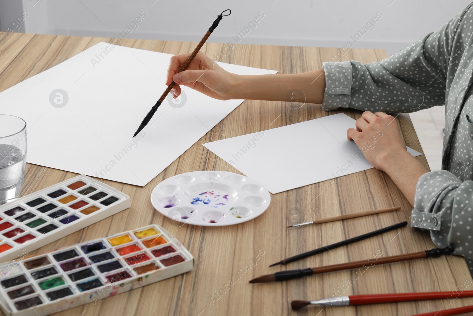 Photo of Woman painting with watercolor on blank paper at wooden table, closeup