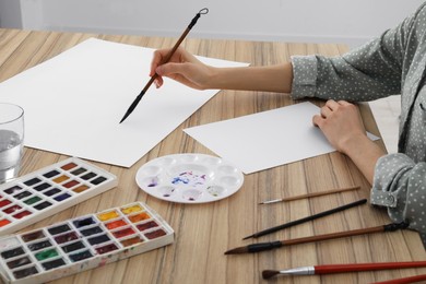 Woman painting with watercolor on blank paper at wooden table, closeup