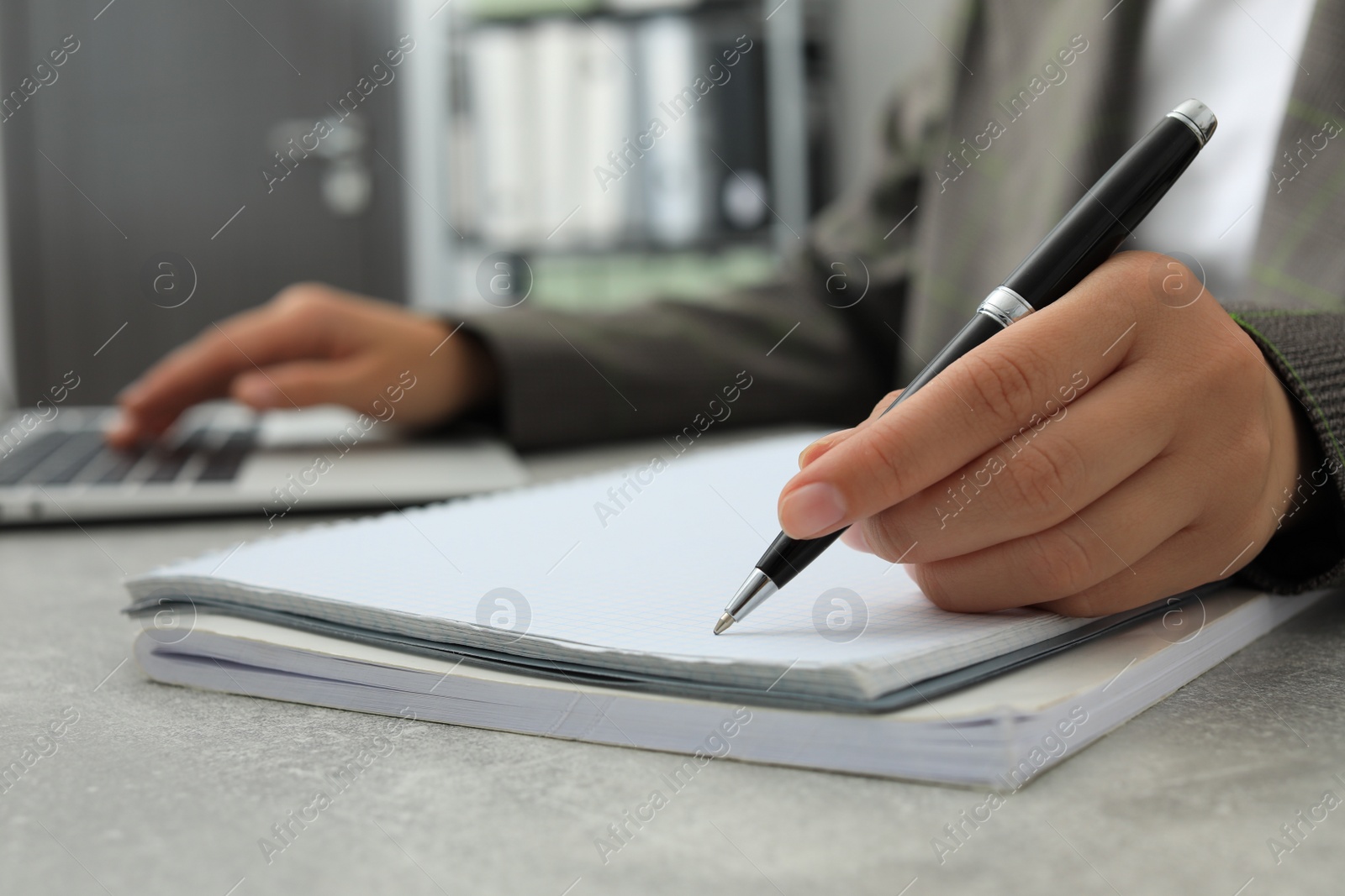 Photo of Woman working with laptop and writing in notebook at table indoors, closeup