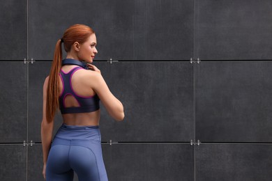 Photo of Beautiful woman in stylish gym clothes with headphones posing near dark grey wall on street, space for text