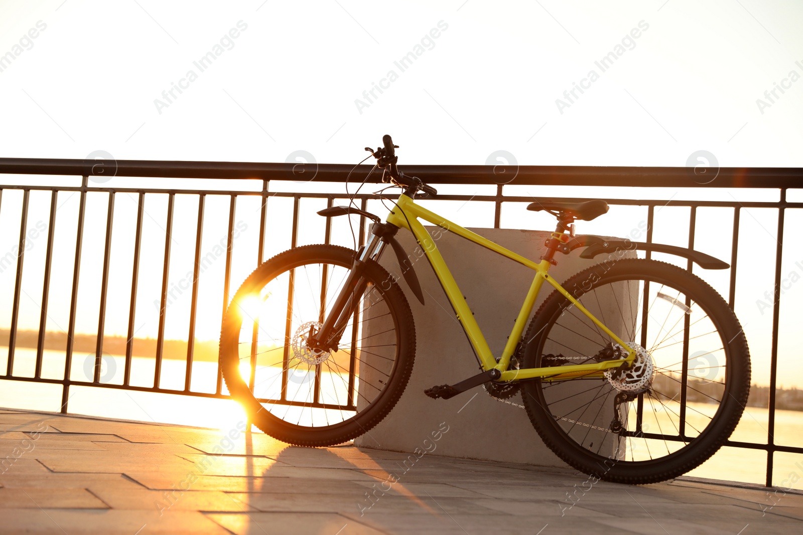 Photo of Yellow bicycle parked near railing on city waterfront at sunset