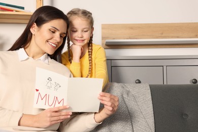Happy woman receiving greeting card from her little daughter at home