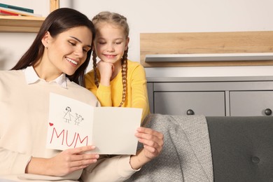 Photo of Happy woman receiving greeting card from her little daughter at home