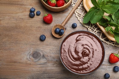 Delicious chocolate cream with berries and mint on wooden table, flat lay. Space for text