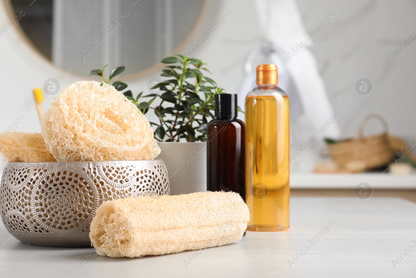 Photo of Natural loofah sponges and personal hygiene products on table in bathroom