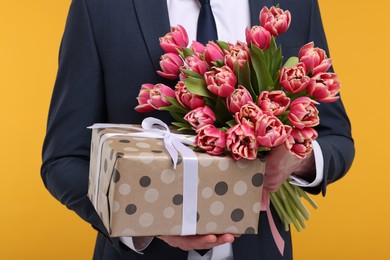 Photo of Man with beautiful bouquet and present on orange background, closeup