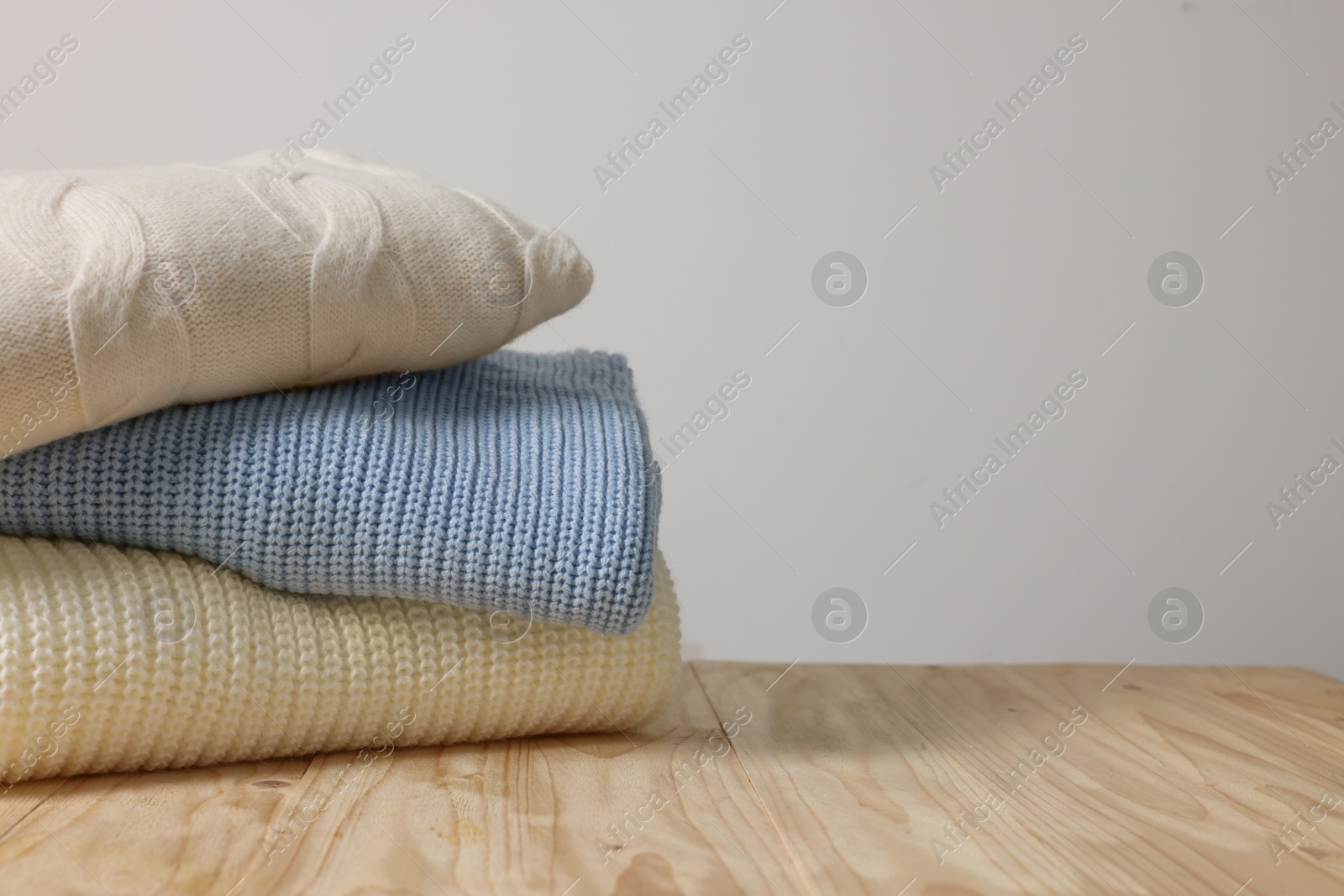 Photo of Stack of casual sweaters on wooden table against light grey background. Space for text