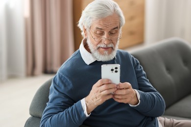 Portrait of happy grandpa with glasses using smartphone indoors