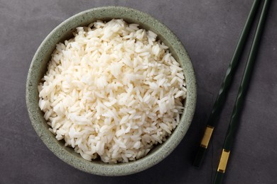 Delicious rice in bowl and chopsticks on grey table, flat lay