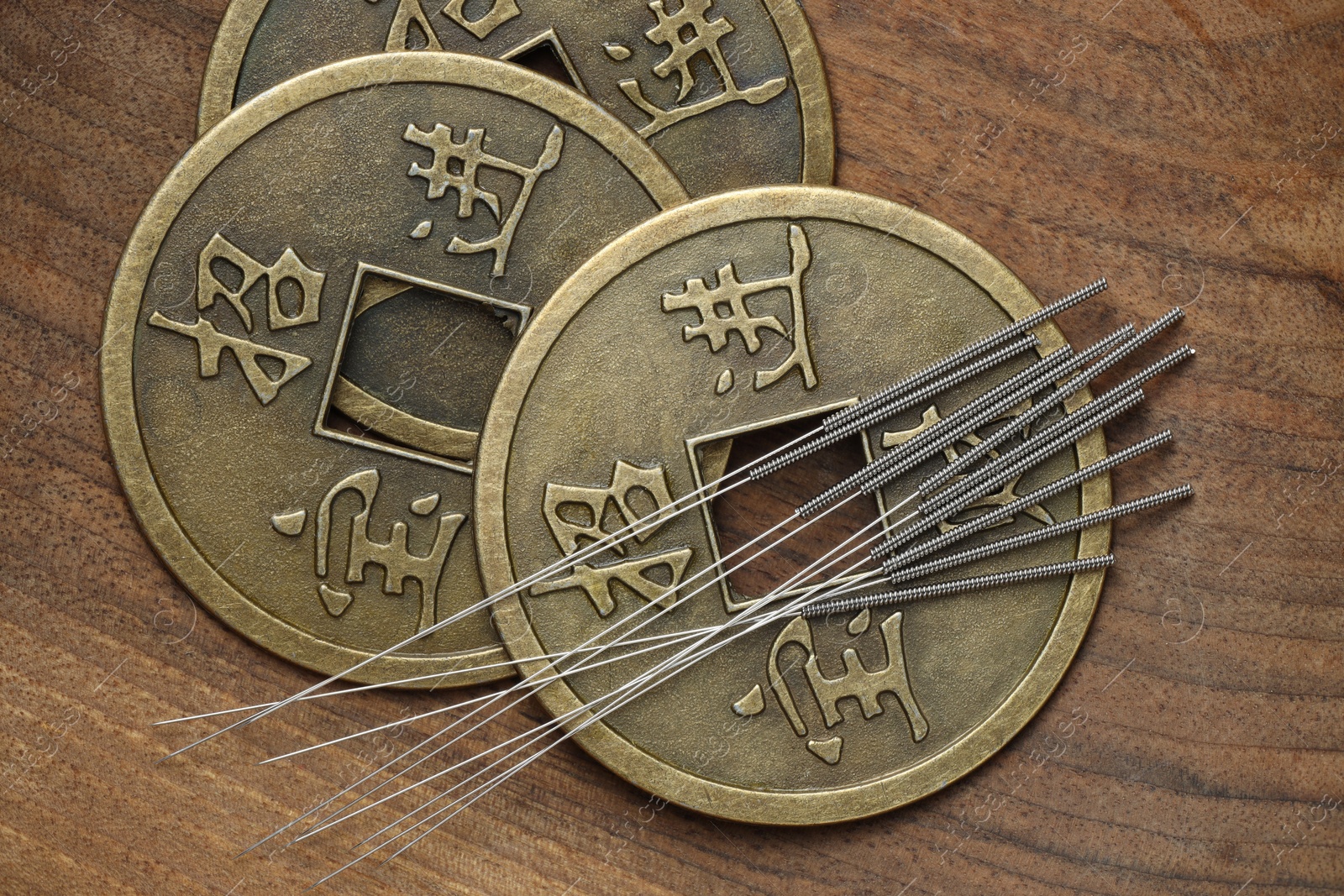 Photo of Acupuncture needles and ancient coins on wooden table, flat lay