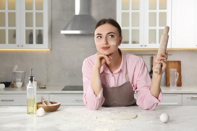 Photo of Beautiful woman with soiled face holding rolling pin at messy table in kitchen