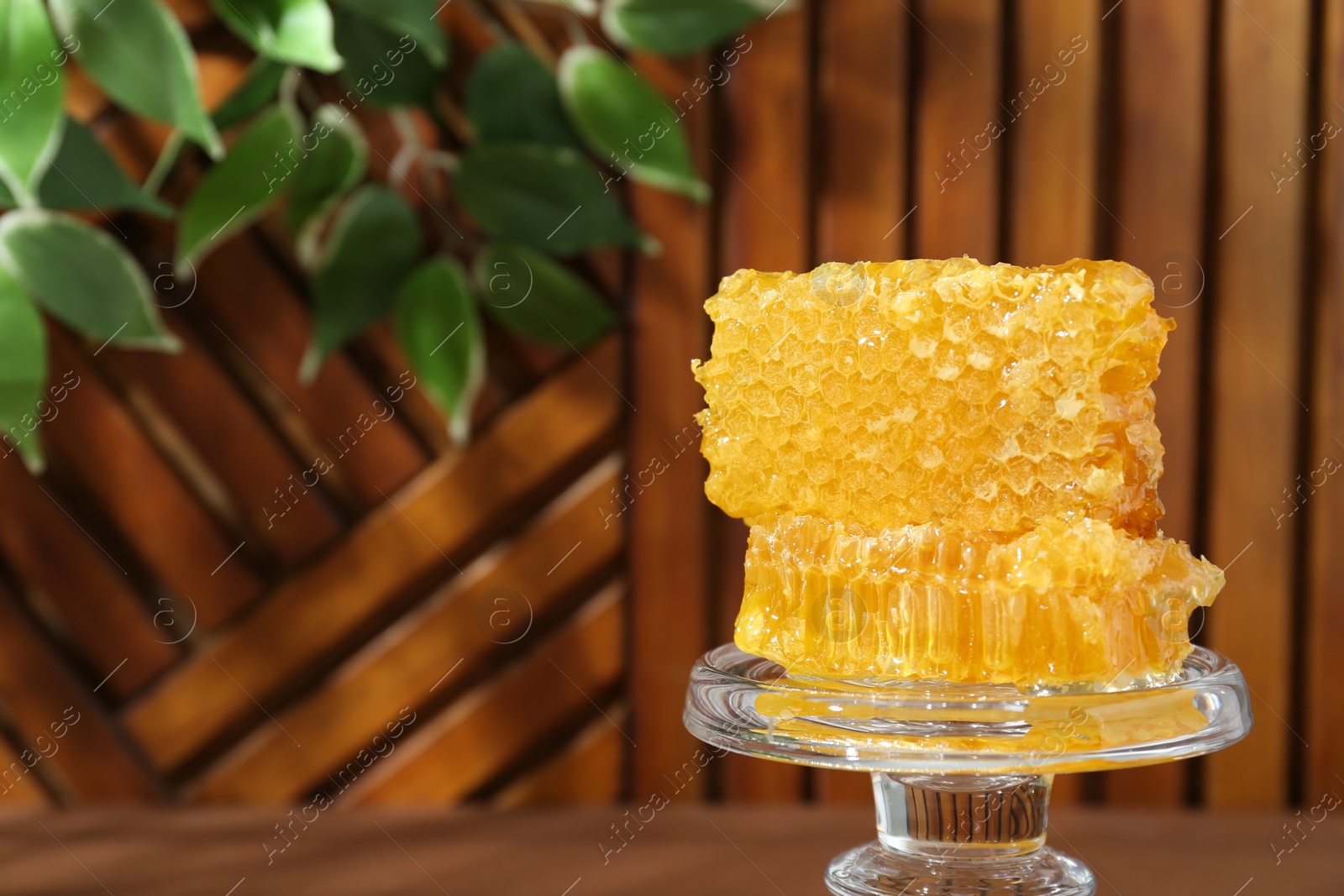 Photo of Glass stand with natural honeycombs on wooden table, closeup. Space for text