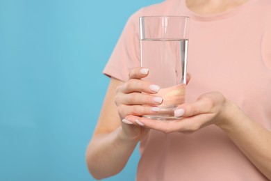 Photo of Healthy habit. Closeup of woman holding glass with fresh water on light blue background, space for text