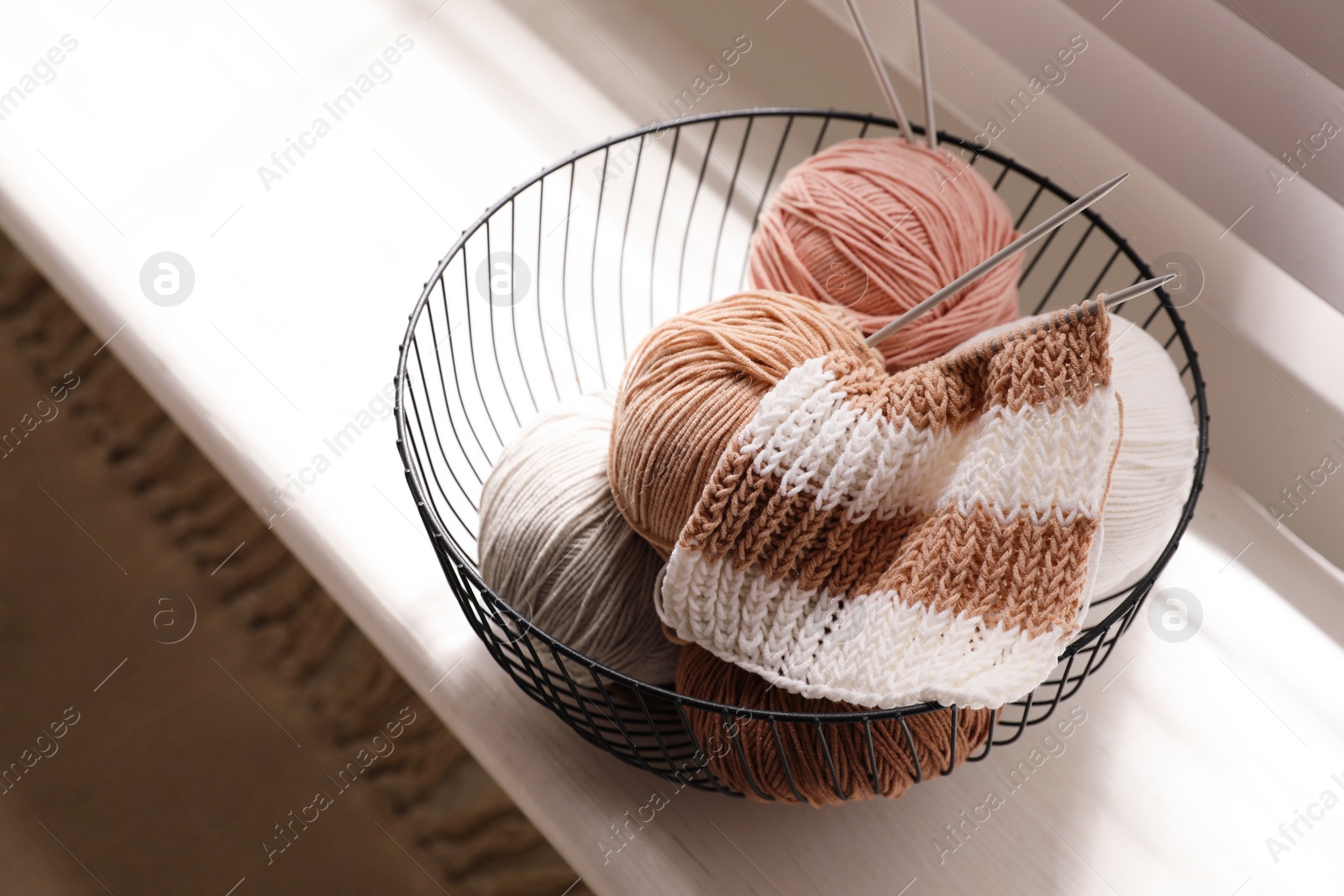 Photo of Yarn balls and knitting needles in metal basket on window sill indoors. Creative hobby