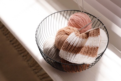 Yarn balls and knitting needles in metal basket on window sill indoors. Creative hobby