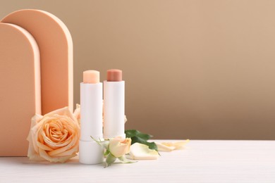 Photo of Stylish presentation of different lip balms with rose flowers on white table, space for text