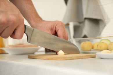 Man cutting garlic at table in kitchen, closeup