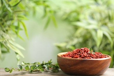 Photo of Bowl of dried goji berries on table against blurred background. Space for text