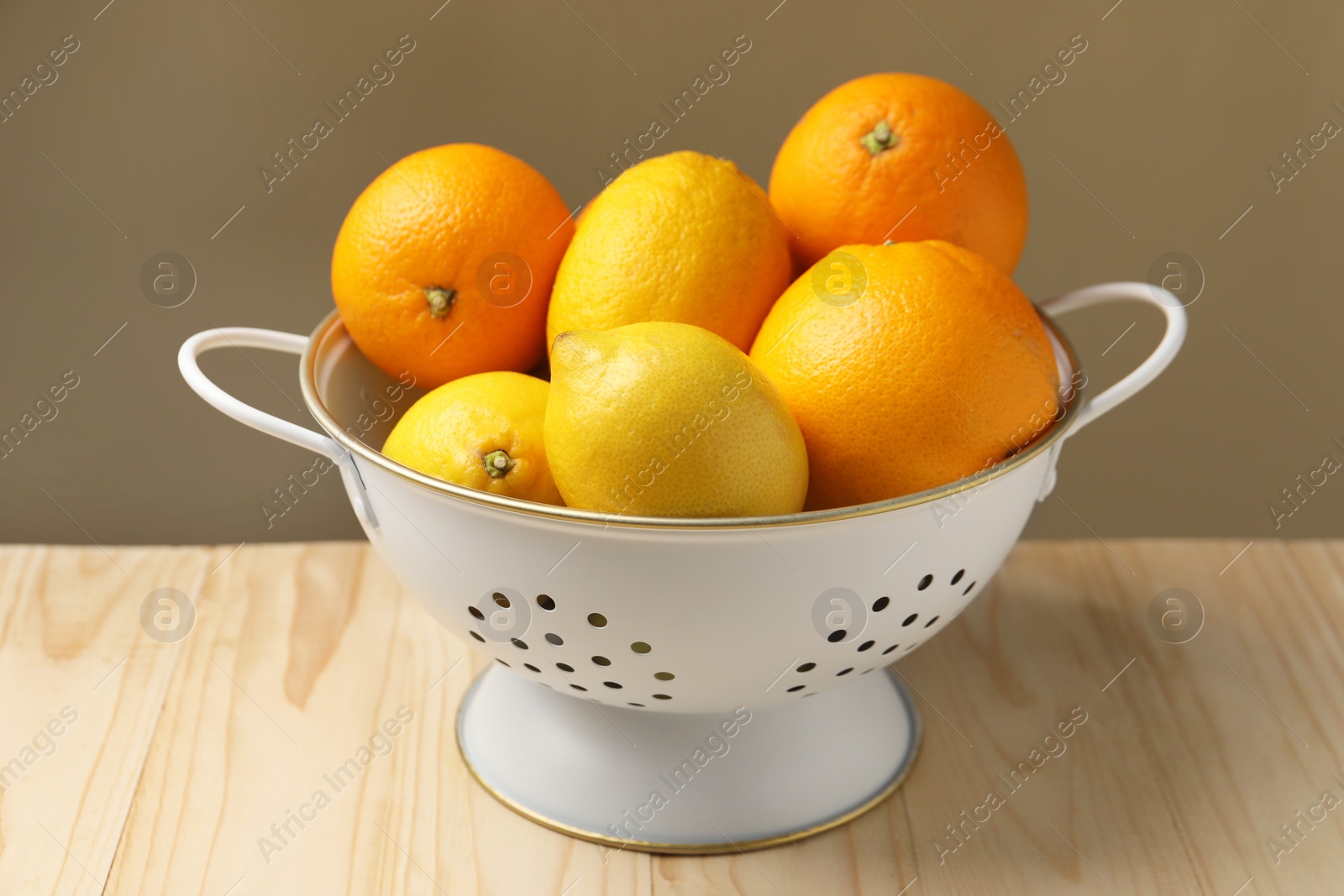 Photo of Colander with fresh citrus fruits on wooden table