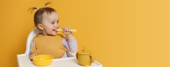 Image of Cute little baby wearing bib while eating on yellow background, space for text. Banner design