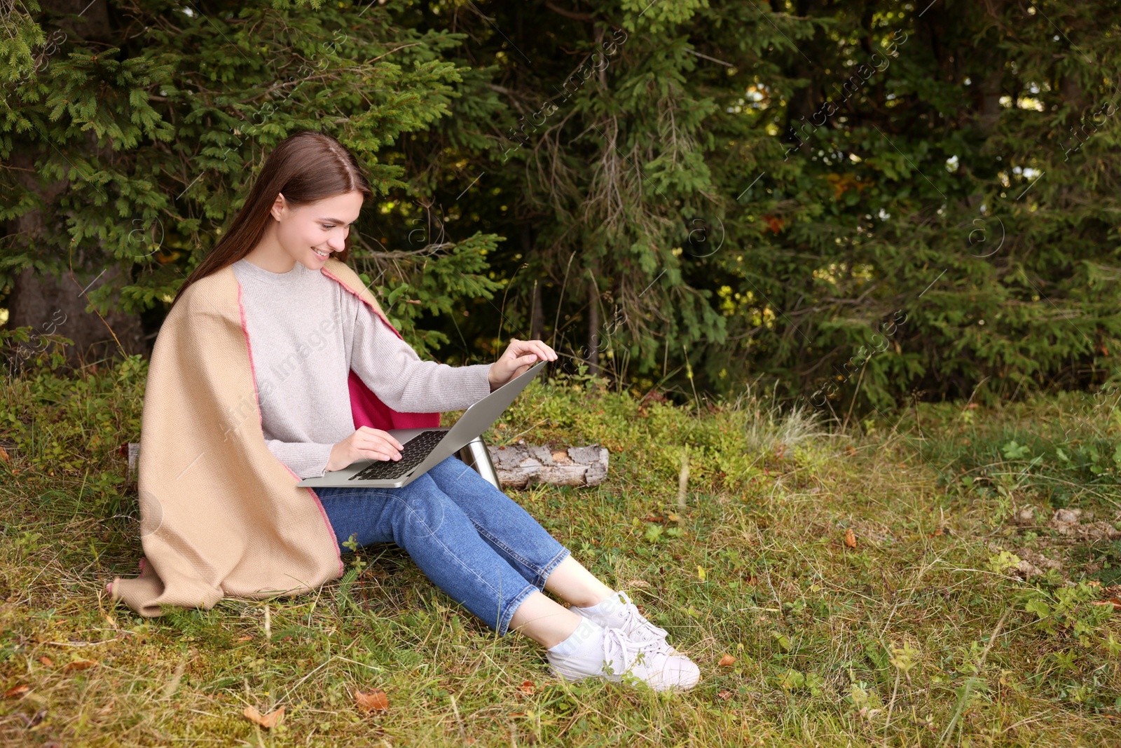 Photo of Young woman working on laptop in forest, space for text