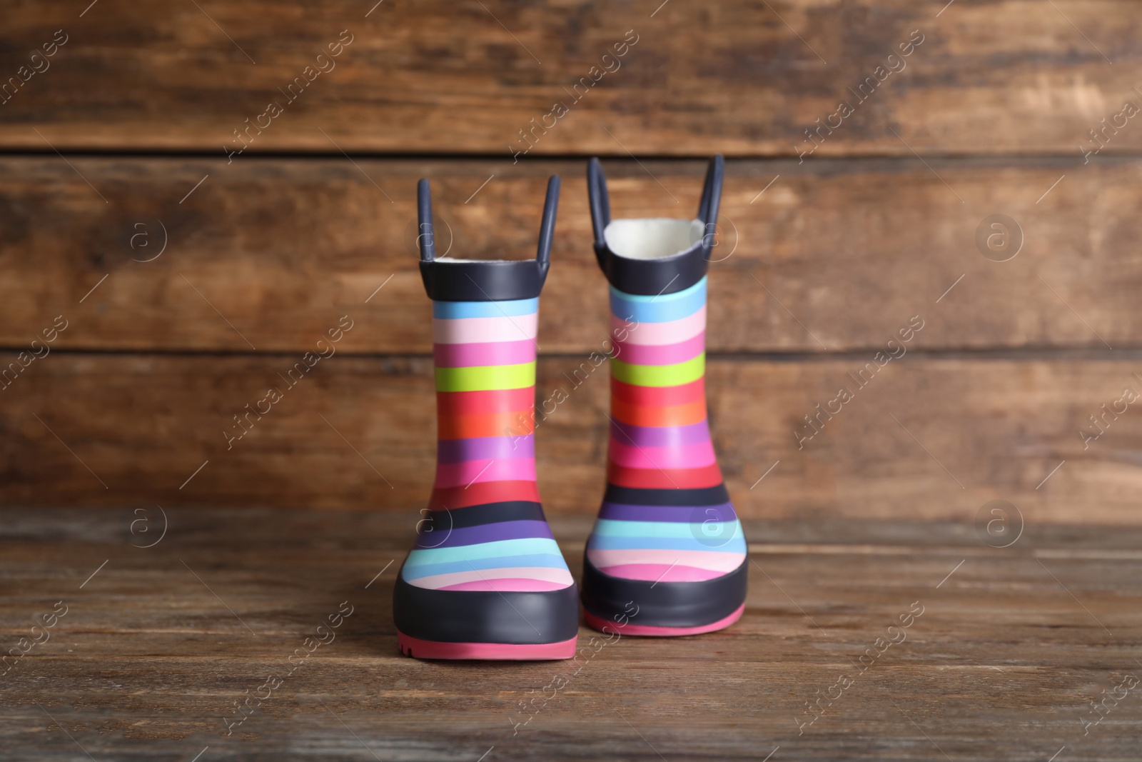 Photo of Pair of striped rubber boots on wooden surface