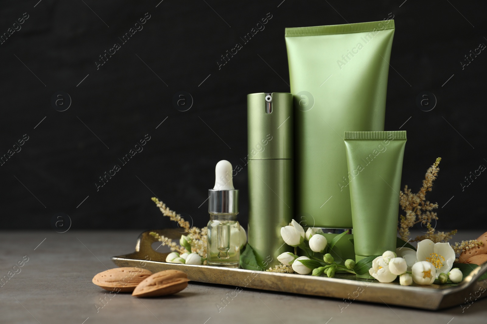 Photo of Set of cosmetic products and flowers on grey table against black background