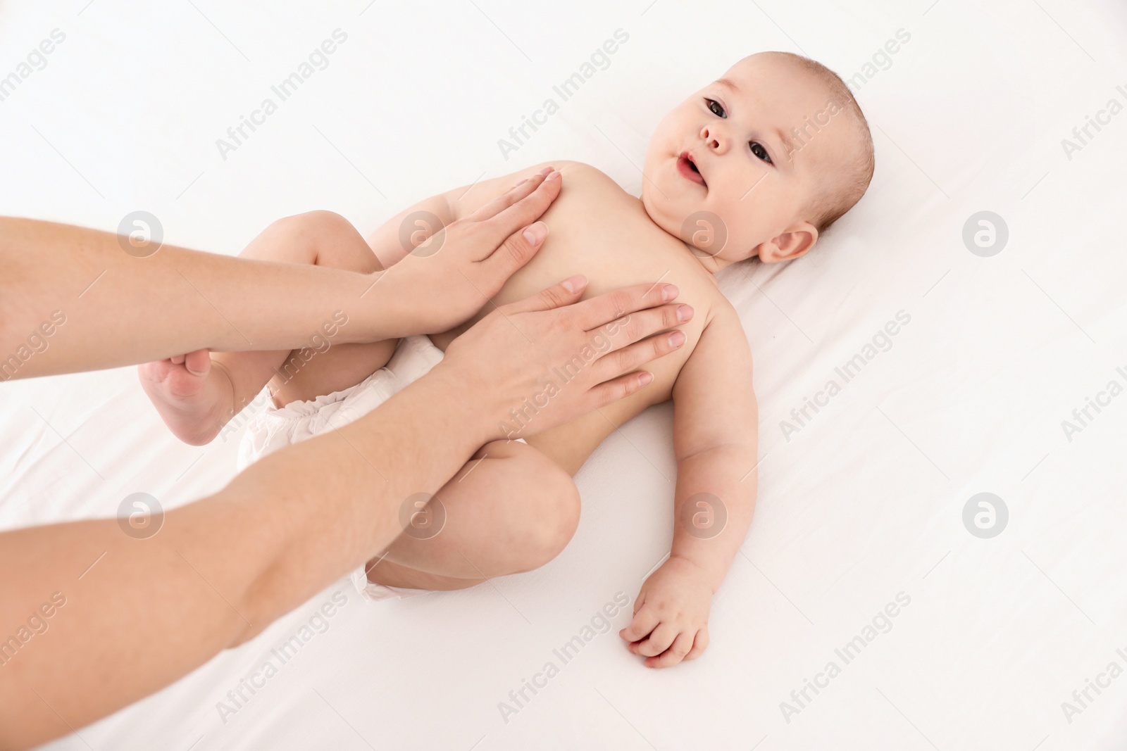 Photo of Mother and her cute child on white bed, above view. Baby massage and exercises