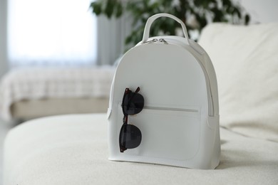 Stylish white backpack with sunglasses in living room, space for text